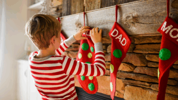 child hanging Christmas stocking on fireplace mantle