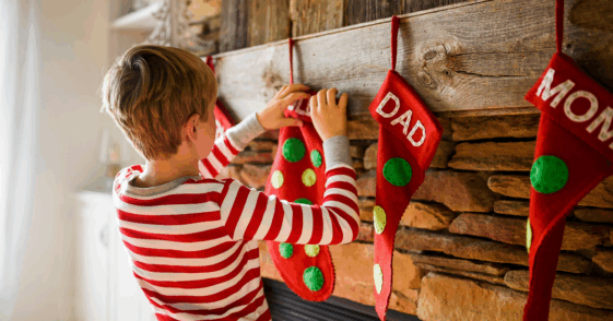 child hanging Christmas stocking on fireplace mantle
