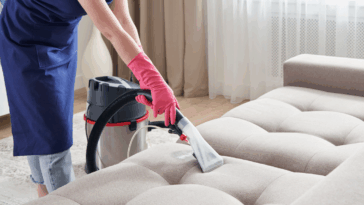 A Woman cleaning a sofa with a vaccum.