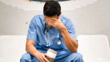 Portrait of a doctor covering his face with his hand.