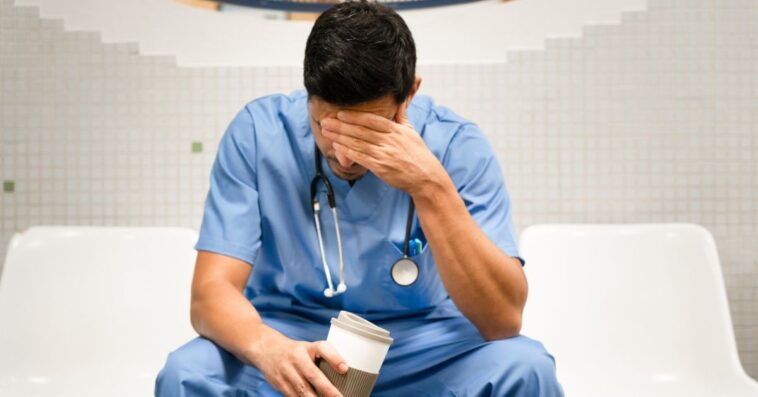 Portrait of a doctor covering his face with his hand.