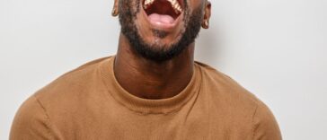 A joyful man is laughing with his head tilted back, showcasing a broad smile. He wears a cozy sweater, creating a cheerful atmosphere.