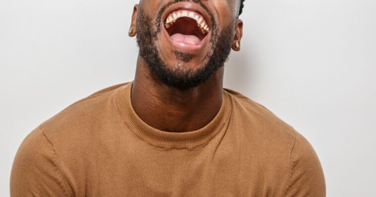 A joyful man is laughing with his head tilted back, showcasing a broad smile. He wears a cozy sweater, creating a cheerful atmosphere.