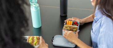 Close-up of two woman coworkers sitting at desk with lunch boxes in office. Healthy food in lunch boxes for female colleagues at work desk.