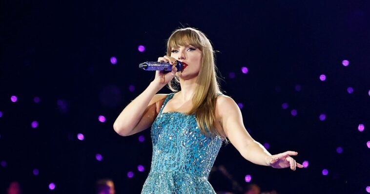 Taylor swift on stage in a blue dress with a microphone in her hand.