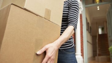 Unidentifiable woman carrying brown boxes from house.