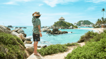 A man standing alone on a beach looking out at the ocean.