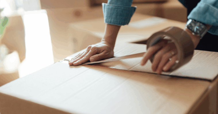 A woman putting tape on a moving box.