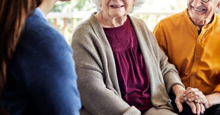 Caregiver with happy senior couple. Smiling elderly male and female are with nurse at home. They are on a home balcony home.