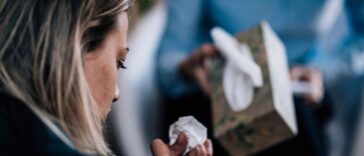 Back shot of a troubled woman crying, talking about her problems. A person in the background offers her tissues.