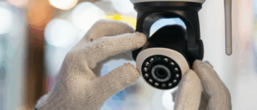 A pair of hands wearing white gloves adjusting a security camera.