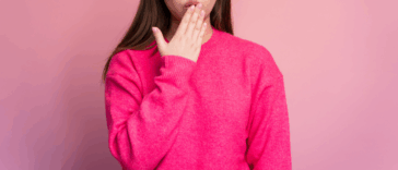 A woman in a pink sweater with her hand covering her mouth.