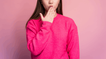 A woman in a pink sweater with her hand covering her mouth.