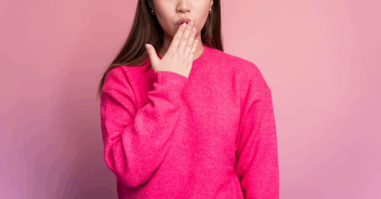 A woman in a pink sweater with her hand covering her mouth.