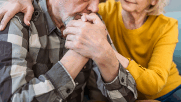 An older man resting his head on his hands and a woman leaning in to comfort him.