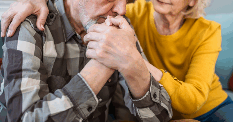 An older man resting his head on his hands and a woman leaning in to comfort him.