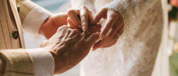 A groom sliding a ring on the finger of a bride.