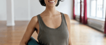 A woman in a tank top holding a yoga mat.