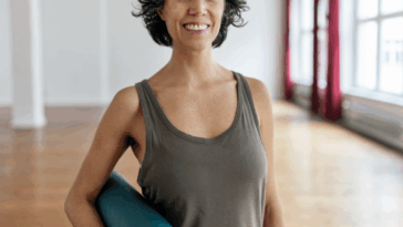 A woman in a tank top holding a yoga mat.