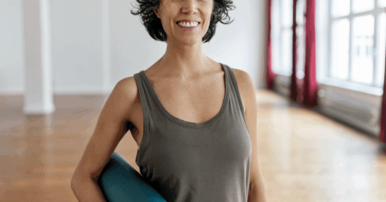 A woman in a tank top holding a yoga mat.
