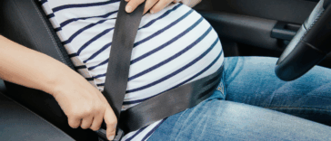 pregnant woman fastening safety belt in her car