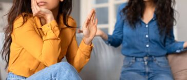 Offended young woman in a yellow top appears upset while conversing with another lady friend in a blue shirt.
