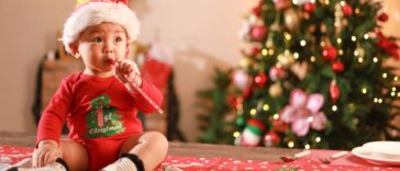 Cute little boy wearing Santa hat sitting on table, playing with toys on Christmas day and Christmas tree background.
