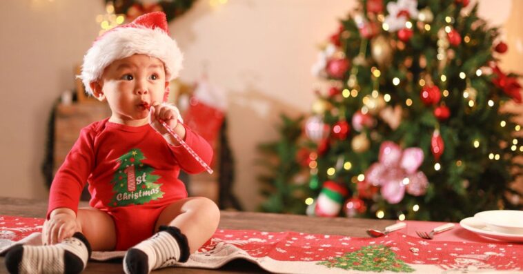Cute little boy wearing Santa hat sitting on table, playing with toys on Christmas day and Christmas tree background.
