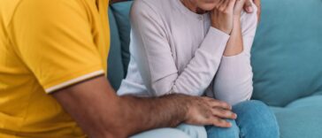 Shot of a mature husband expressing empathy and compassion to his sad frustrated wife. They sit huddled on their couch at home.