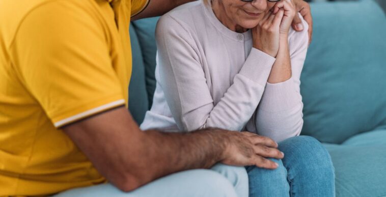 Shot of a mature husband expressing empathy and compassion to his sad frustrated wife. They sit huddled on their couch at home.