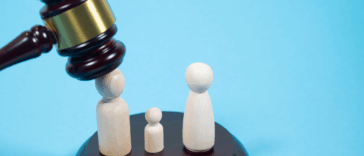 A gavel falling down on a figurine standing next to a smaller figurine and an identical figurine.