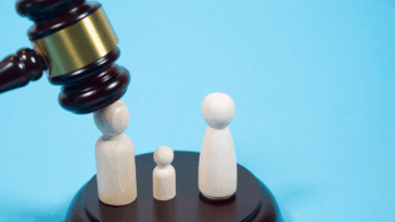 A gavel falling down on a figurine standing next to a smaller figurine and an identical figurine.