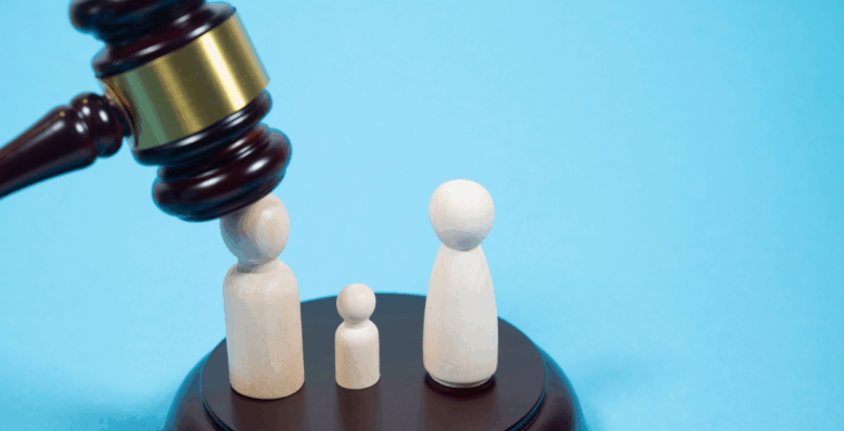A gavel falling down on a figurine standing next to a smaller figurine and an identical figurine.