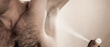 Mid studio shot of an adult man spraying deodorant.