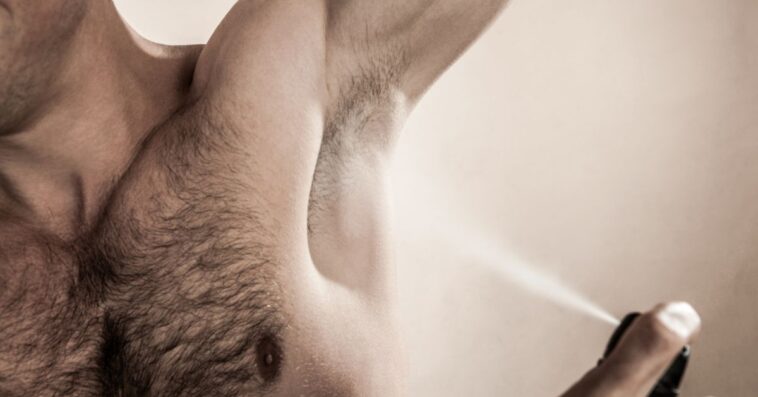 Mid studio shot of an adult man spraying deodorant.