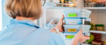 Back view shot of a woman taking or putting lunch boxes cooked in advance, ready to be served into fridge. Containers with eco healthy food. Pre-cooking concept.