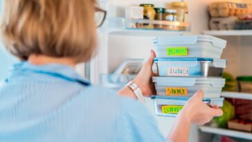 Back view shot of a woman taking or putting lunch boxes cooked in advance, ready to be served into fridge. Containers with eco healthy food. Pre-cooking concept.