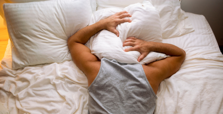 A man in bed with his head covered in pillows.
