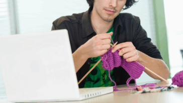 A man knitting at his office desk.