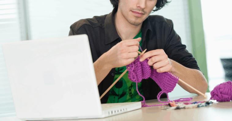 A man knitting at his office desk.