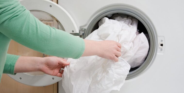 Woman taking sheet from washing machine.