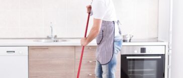 Young handsome man mopping tiled floor in kitchen. Husband housework concept.