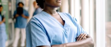 Contemplating female nurse with arms crossed looks through a window in the hospital.
