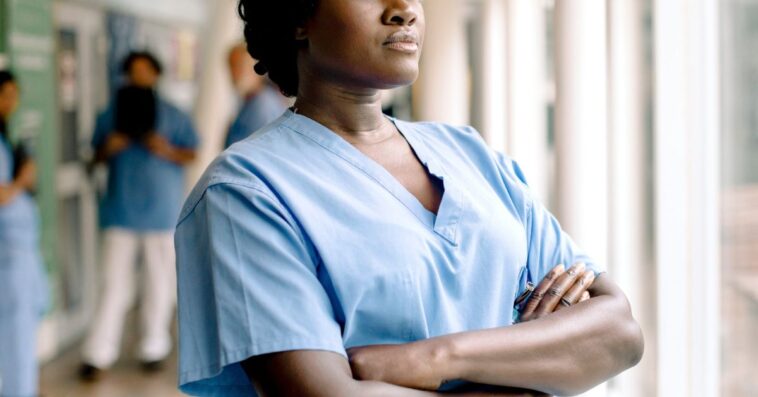 Contemplating female nurse with arms crossed looks through a window in the hospital.