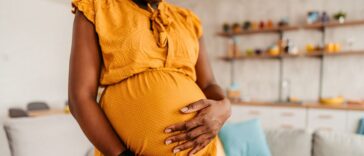 Portrait of beautiful pregnant mother holding her pregnant belly at home. Close-up.