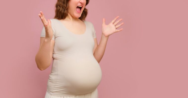 A screaming pregnant woman on a studio pink background.