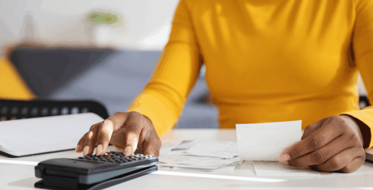 A woman sitting at a table with a calculator and paper receipts.