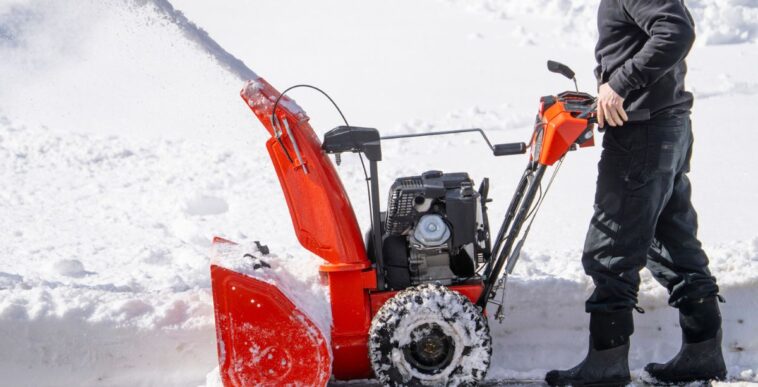 Unidentifiable man removing snow on the driveway of the house by snow blower.