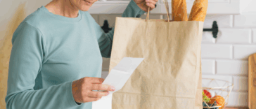 A woman at a counter looking at a list next to a bag full of groceries.
