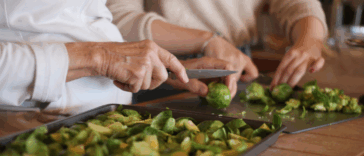 Two women cutting up brussell sprouts at a kitchen counter.